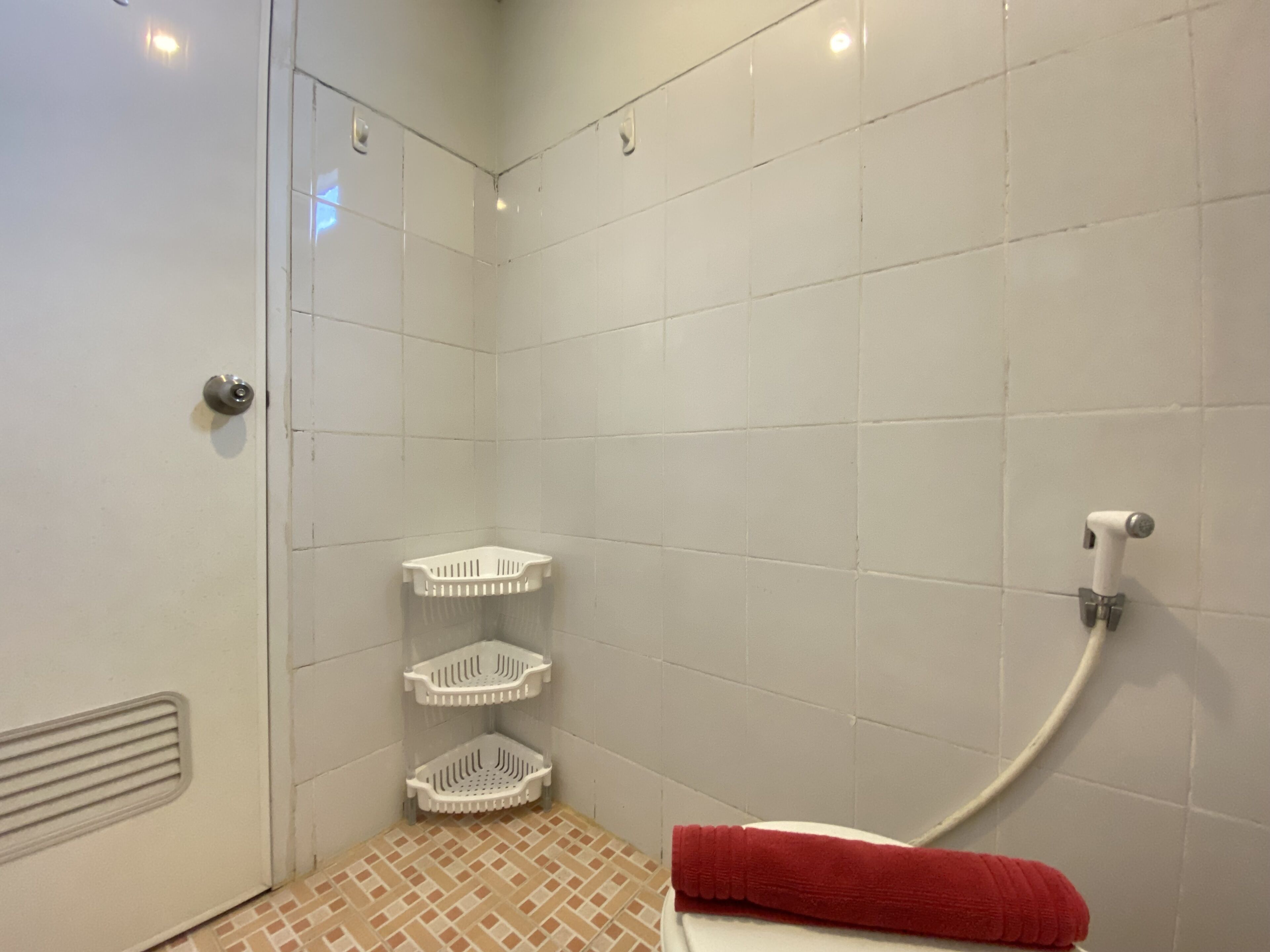 A bathroom with white tiled walls, a shower area, and a toilet with a red towel.