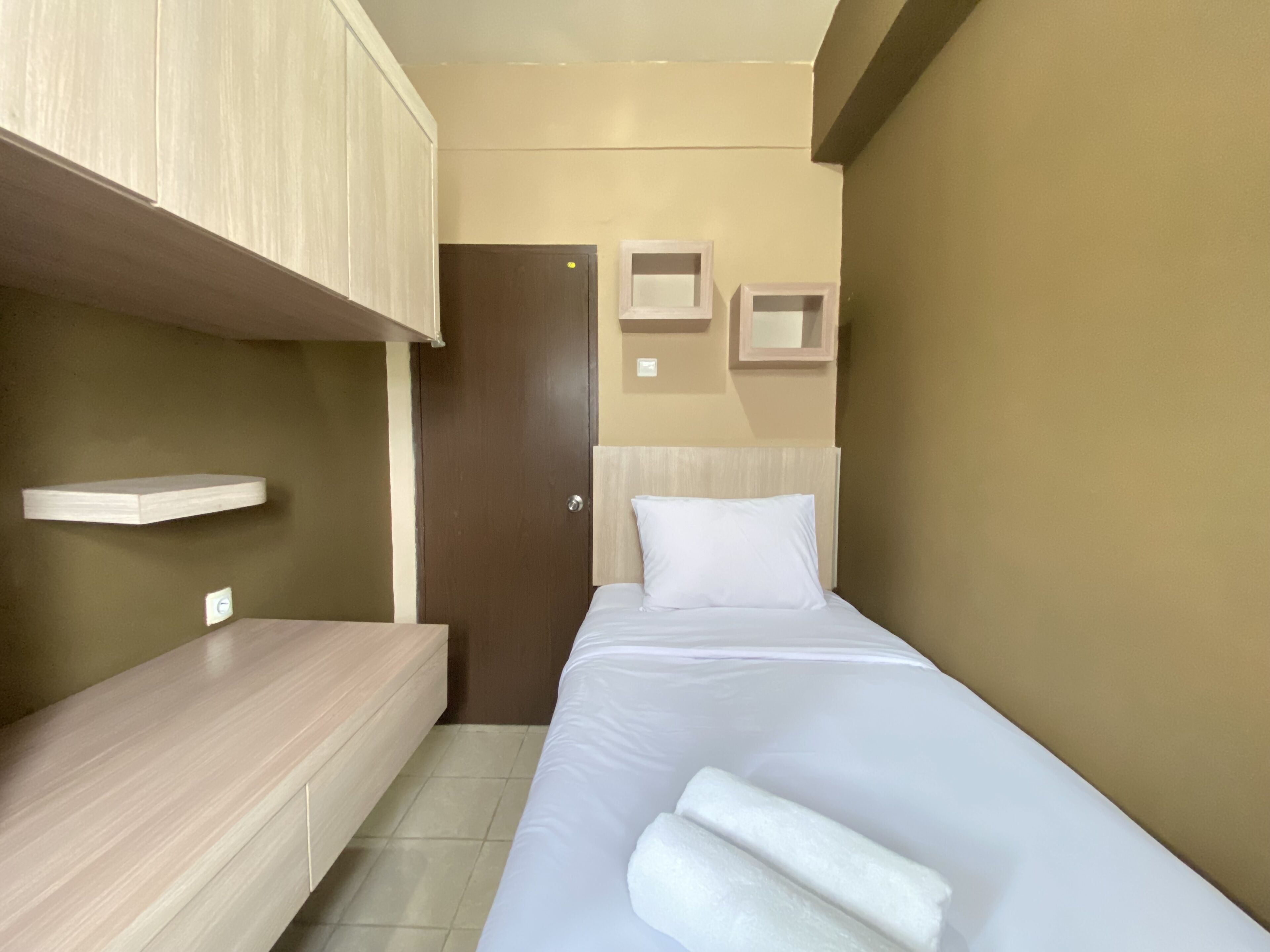 A modern hotel room with a bed, a wooden bench, a wardrobe, and a small shelf.
