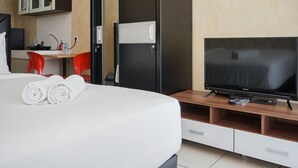 A hotel room with a bed, a TV, a desk with a chair, and a wardrobe. - Fancy And Comfy Studio Apartment At M-Town Residence (Gading Serpong)