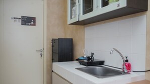 A compact kitchen with a white countertop, a stainless steel sink, and a microwave above cabinets. - Fancy And Comfy Studio Apartment At M-Town Residence (Gading Serpong)