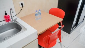 A kitchen with a sink, a wooden table, two red chairs, and two water bottles on the table. - Fancy And Comfy Studio Apartment At M-Town Residence (Gading Serpong)