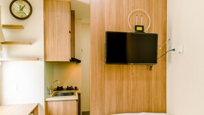 Ein kleines Hotelzimmer mit einem Holzkabinett, einer kleinen Küchenzeile, einem an der Wand befestigten Flachbildfernseher und einem ordentlich bezogenen Bett.