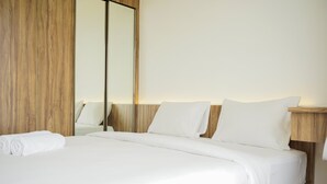 A neatly made bed with white linens and pillows, a wooden headboard, and a large mirror on the wall. - Fully Furnished With Modern Design 2Br At Sky House Bsd Apartment (Pagedangan)