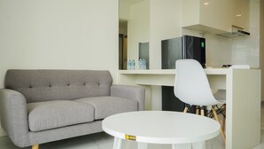 A modern room with a grey sofa, a white table, and a black refrigerator. - Fully Furnished With Modern Design 2Br At Sky House Bsd Apartment (Pagedangan)