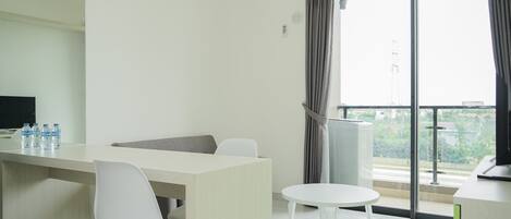 Una habitación de hotel moderna con un balcón grande, una zona de comedor con mesa y sillas, y un televisor a la izquierda.