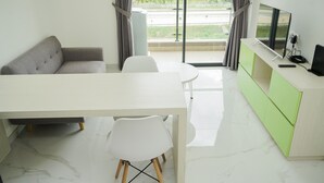 A modern living room with a sofa, a dining table, a TV, and a green cabinet. - Fully Furnished With Pleasure Tidy 2Br At Sky House Bsd Apartment (Pagedangan)