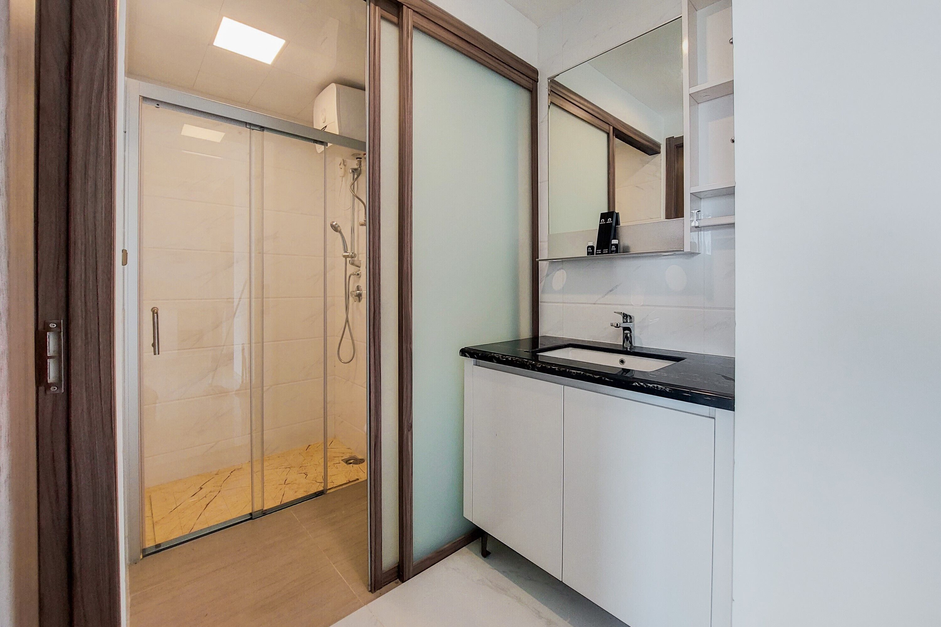 Un baño moderno con cabina de ducha de vidrio, un lavamanos con encimera negra y un espejo grande sobre el lavamanos.