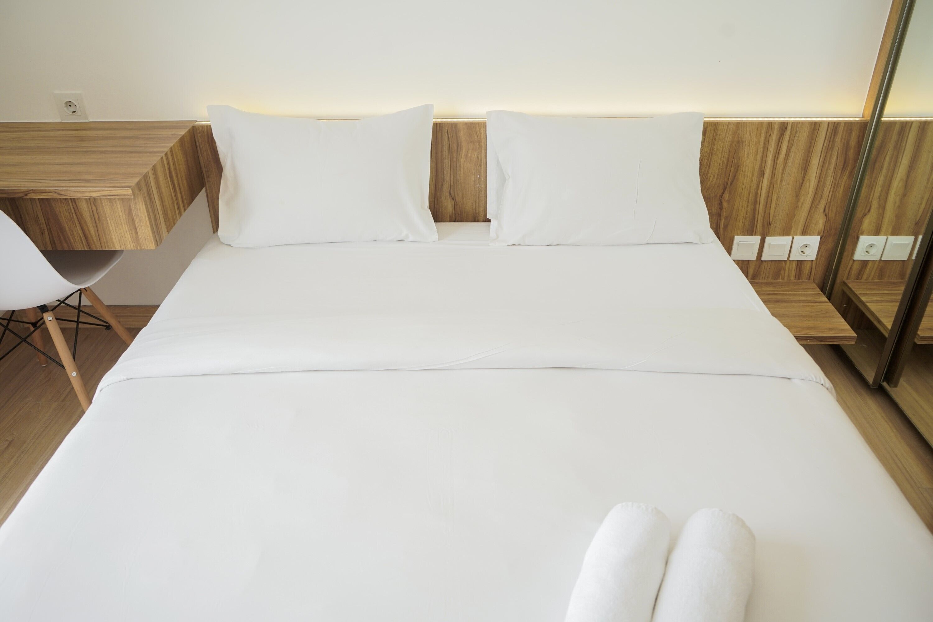 A modern hotel room with a large bed, wooden headboard, and a small desk with a chair.