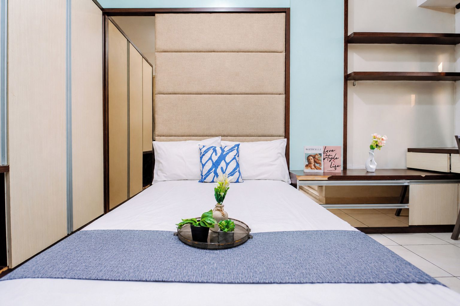A neatly arranged hotel room with a bed, bedside table, and a small desk area.