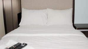 A neatly made bed with white linens and pillows, a remote control on the bed, and a nightstand with a lamp. - Fancy Studio At Springlake Summarecon Bekasi Apartment (Bekasi)