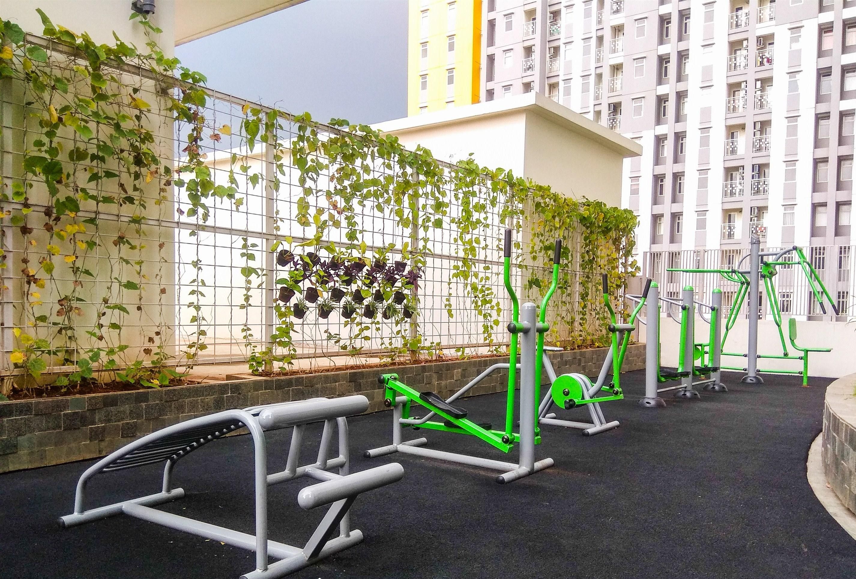 An outdoor gym area with exercise equipment, surrounded by a climbing wall with greenery.