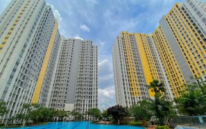 Een hoog appartementencomplex met meerdere balkons, een zwembad en veel groen eromheen.