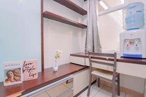 A hotel room with a wooden desk, a water dispenser, a chair, and a vase with flowers.
