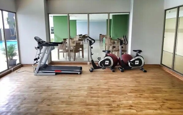 Une salle de sport équipée d’un tapis de course, de vélos d’appartement et d’un rameur.