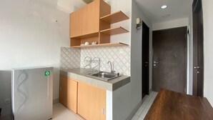 A compact kitchen with a built-in refrigerator, a sink, wooden cabinets, and a dining table. - Bright And Relaxing 2Br At Mekarwangi Square Bandung (Bandung)
