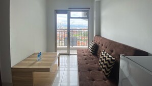 A living room with a brown sofa, a wooden coffee table, and a view through a glass door to an outdoor balcony. - Bright And Relaxing 2Br At Mekarwangi Square Bandung (Bandung)