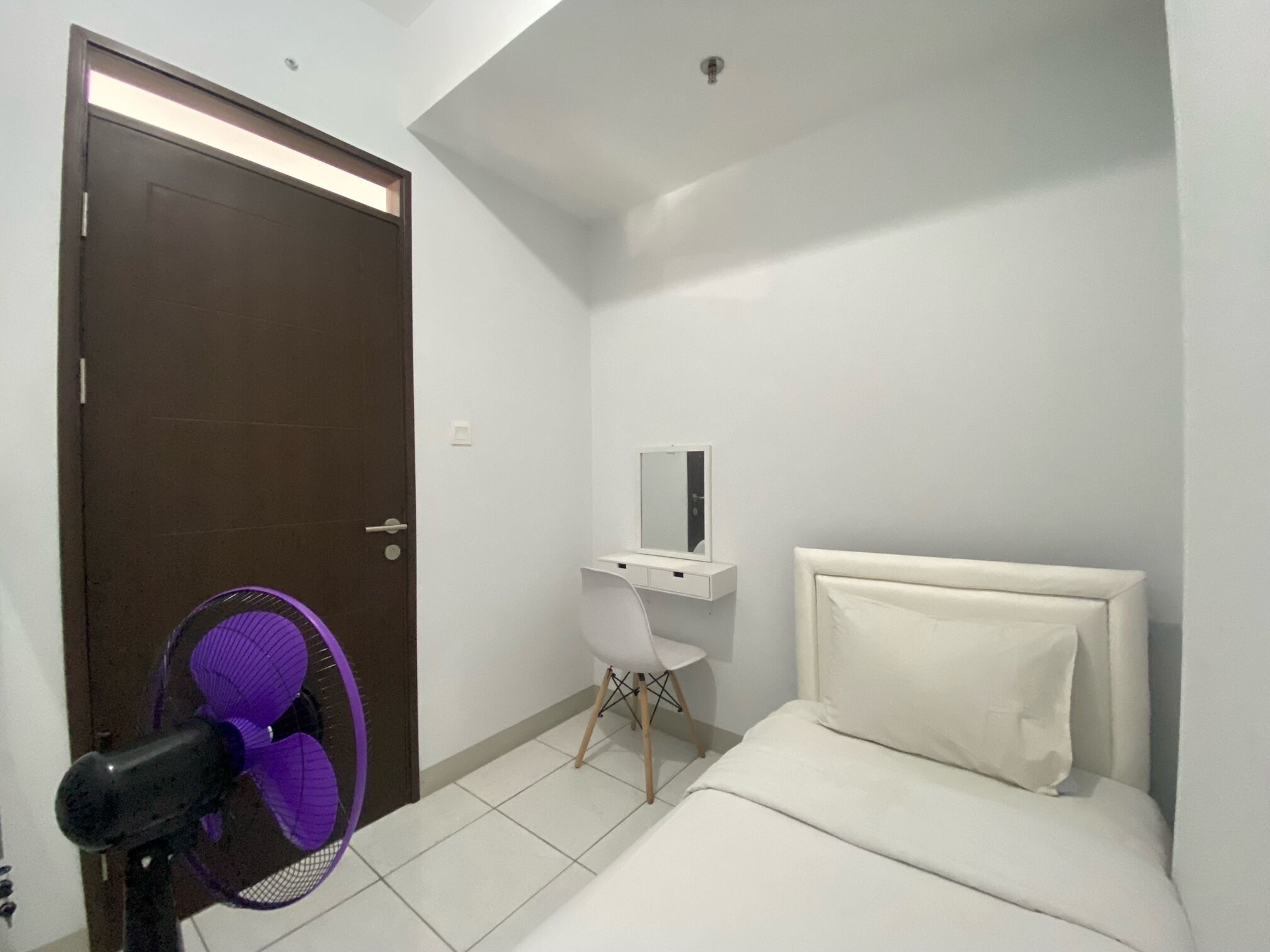 Une petite chambre à coucher moderne, avec un lit, une table de chevet blanche, un miroir et un ventilateur violet.