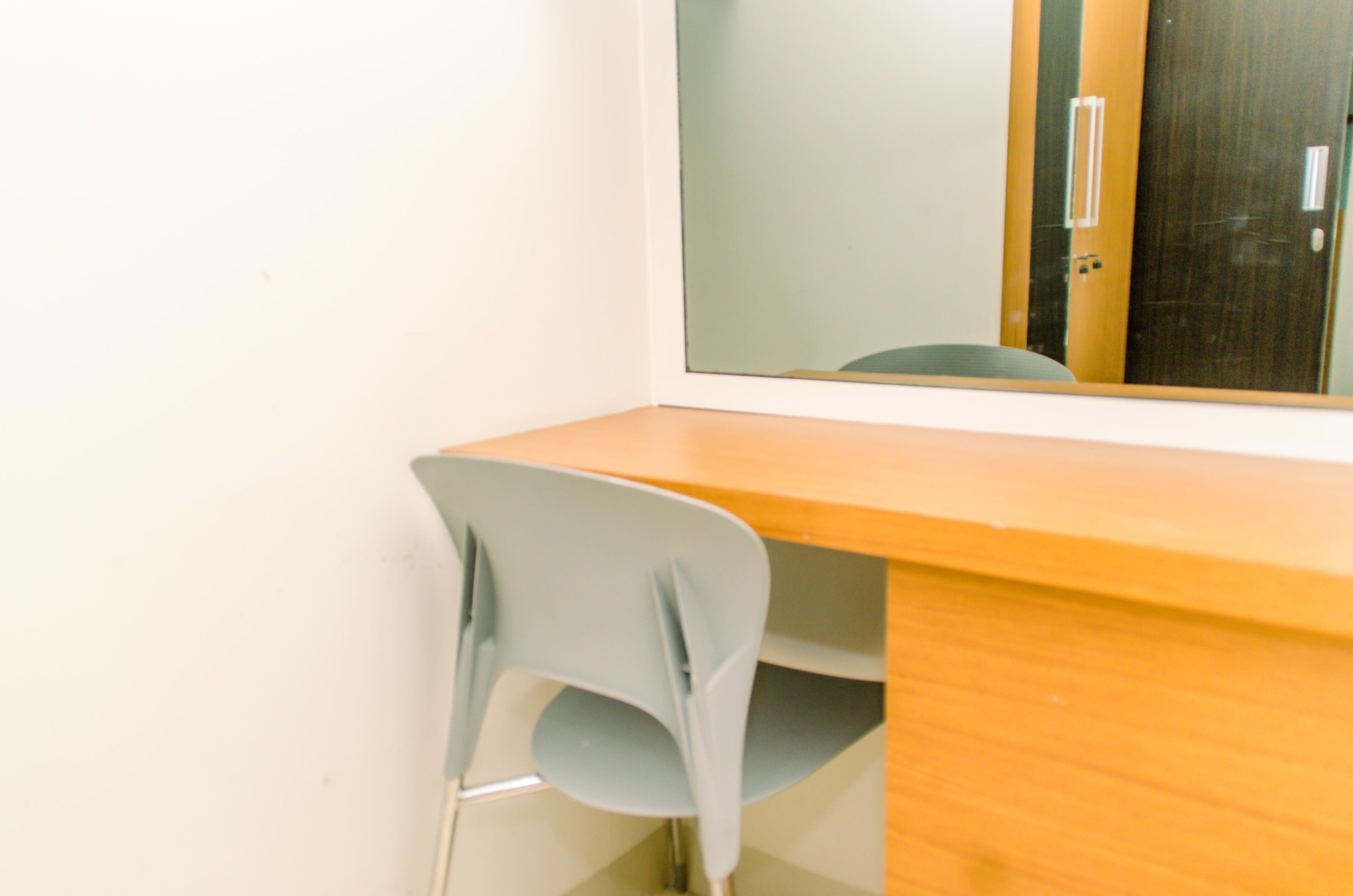Un bureau en bois, une chaise bleu clair, un miroir et une porte à l’arrière-plan.