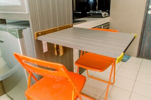 Uma cozinha compacta com bancada cinza, duas cadeiras laranja e uma pequena mesa.