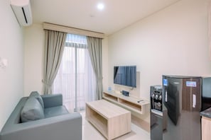 A modern living room with a grey sofa, a wooden coffee table, a flat-screen TV, a refrigerator, and a water dispenser.