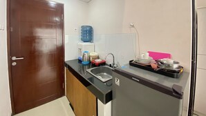 A compact kitchen with a brown door, a water dispenser, a kettle, a coffee maker, a sink, and a microwave. - Cozy Studio Apartment At Gateway Pasteur Bandung (Cimahi)