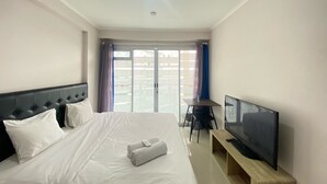 A hotel room with a bed, a TV, a small table, and a window with curtains. - Cozy Studio Apartment At Gateway Pasteur Bandung (Cimahi)