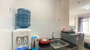 A kitchenette with a water dispenser, kettle, and a small sink. - Cozy Studio Apartment At Gateway Pasteur Bandung (Cimahi)
