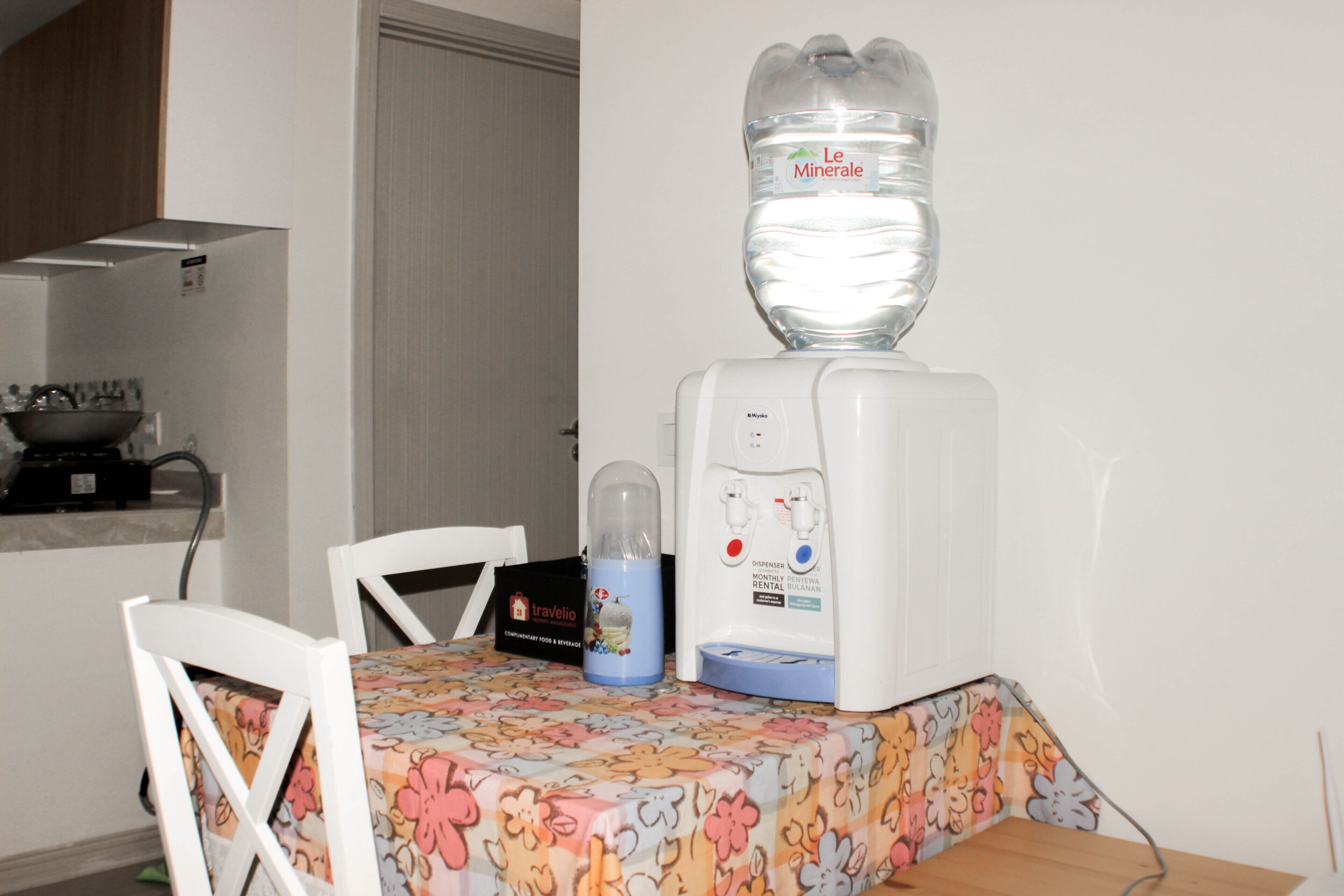 Uma cozinha com dispensador de água, chaleira e uma mesa com cadeiras.
