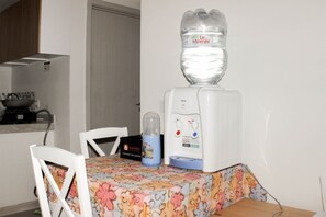 A kitchen with a water dispenser, a kettle, and a table with chairs. - Nice And Spacious 3Br At Meikarta Apartment (Cikarang)