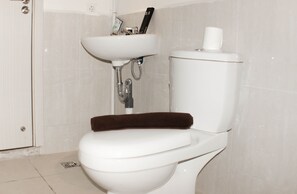 A bathroom with a toilet, sink, and a toilet paper holder. - Nice And Spacious 3Br At Meikarta Apartment (Cikarang)