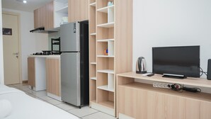 A compact kitchen with a refrigerator, stove, and microwave. There is a television on a wooden shelf and a power strip below it. - Nice And Comfort Studio At M-Town Residence Apartment (Gading Serpong)