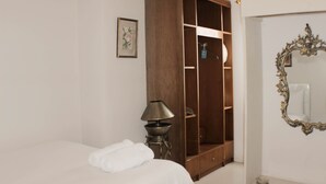 A bedroom with a bed, a wooden wardrobe, a lamp, and a mirror. - Minimalist And Homey 1Br At Bassura City Apartment (Jakarta)