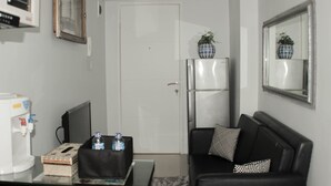 A compact living space with a black sofa, a small coffee table, a refrigerator, and a television on a stand. - Minimalist And Homey 1Br At Bassura City Apartment (Jakarta)