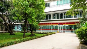 A modern building with a red and yellow facade, large windows, and a well-maintained courtyard with trees and a tiled walkway.