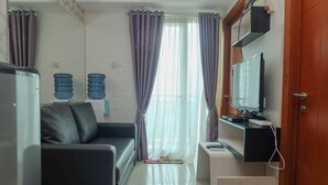A modern living room with a black sofa, a small white table, a TV on a stand, and a door with a mirror.