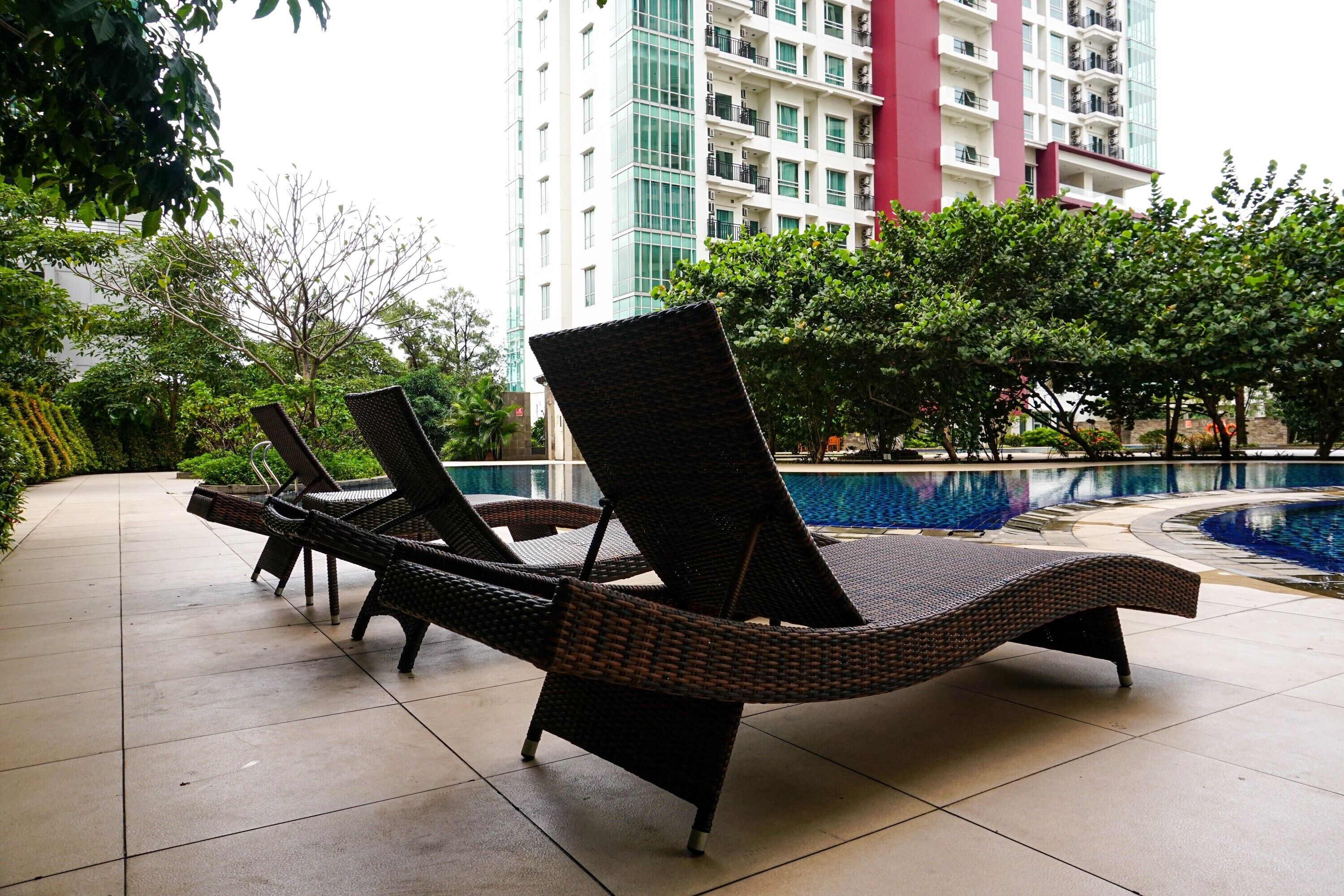 Outdoor lounge chairs by a poolside with a modern building in the background.