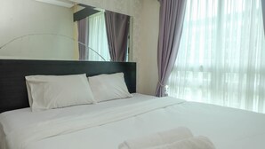 A neatly made bed with white linens, a dark headboard, and a folded towel on the bed.