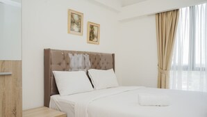 A neatly made bed with white linens, a wooden nightstand, and two framed pictures on the wall. - Comfrot 2Br At Sky House Bsd Apartment (Pagedangan)
