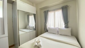 A hotel room with a bed, a large mirror, and a window with curtains. - Cozy 2Br At Pinewood Apartment Jatinangor (Cileunyi)