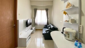 A modern living room with a flat-screen TV, a sofa, a coffee maker, and a water dispenser on the counter. - Cozy 2Br At Pinewood Apartment Jatinangor (Cileunyi)