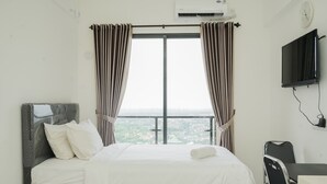 Habitación de hotel con cama, escritorio, silla y un amplio ventanal con cortinas.