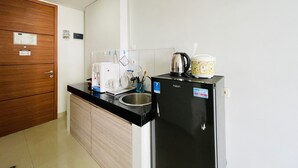 Een kleine keuken met een zwarte koelkast, een koffiezetapparaat, een waterkoker en een rijstkoker op het aanrecht.