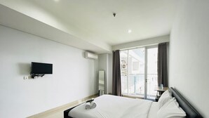 Een hotelkamer met een bed, een aan de muur bevestigde televisie, een airconditioning en een raam met gordijnen.