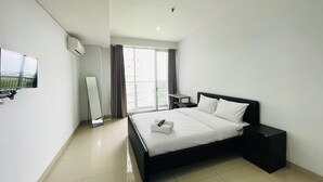 Een moderne hotelkamer met een groot bed, een flatscreen televisie aan de muur, een kleintje tafeltje en een raam met gordijnen.