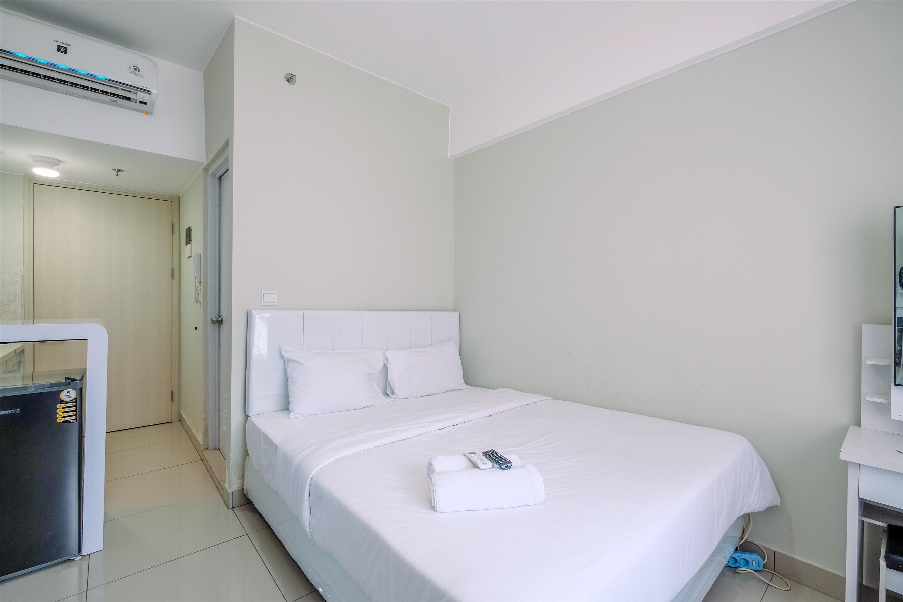 A hotel room with a bed, a white headboard, a remote control, and a white towel on the bed.
