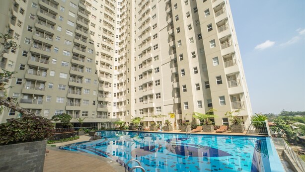 A high-rise building with a swimming pool on the ground level. - Spacious Studio Room Apartment At Parahyangan Residence (Bandung)