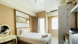 A hotel room with a bed, a bedside table with a mirror, a dresser, an air conditioning unit, and a window with curtains. - Spacious Studio Room Apartment At Parahyangan Residence (Bandung)