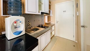 A kitchen with white cabinets, a black countertop, a sink, and a water dispenser. - Spacious Studio Room Apartment At Parahyangan Residence (Bandung)