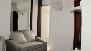 A modern living room with a grey sofa, a large mirror, and two wall-mounted fans. - Comfort 2Br Apartment At Mediterania Palace Residence (Jakarta)