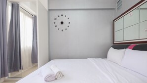 A hotel room with a bed, a wall clock, and a window with curtains. - Comfort And Warm 2Br At Bassura City Apartment (Jakarta)
